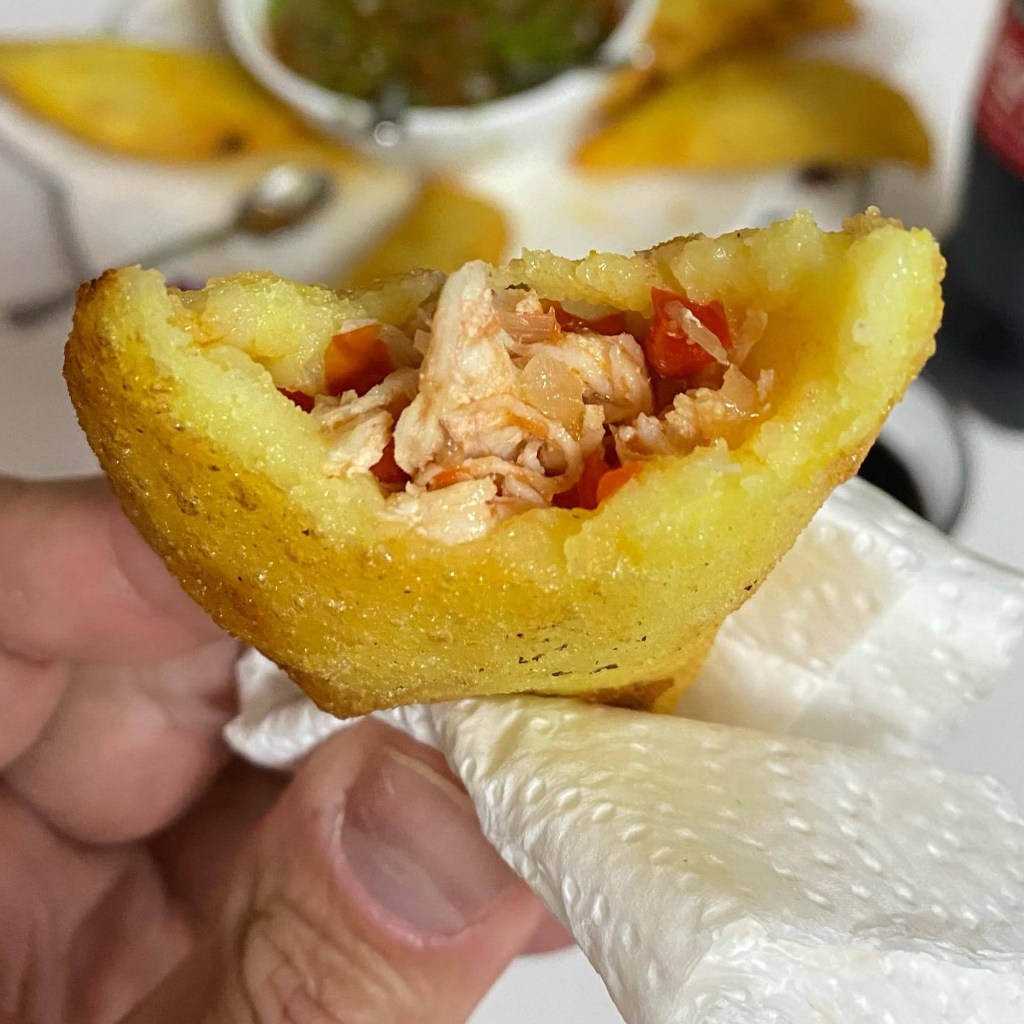 A close-up shot of a Colombian empanada with chicken and fillings. The empanada has been bitten into and you can see the chicken filling inside. 