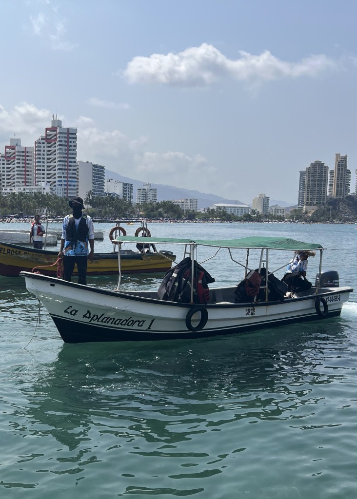 A small boat, or lancha as they call them in Colombia, is in the bay of Rodadero, Colombia. Skyscrapers and mountains are in the background. 