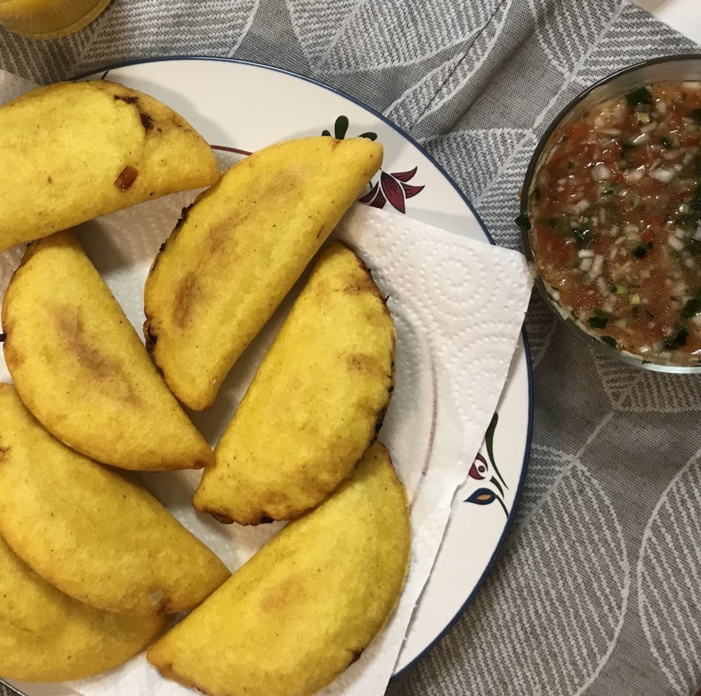 A plate of golden Colombian empanadas is next to a bowl of spicy sauce, called picante. 